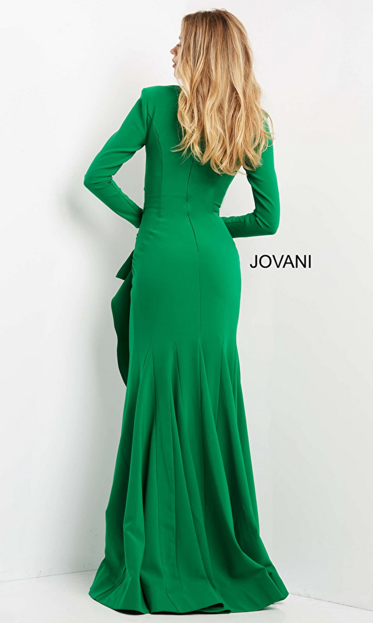 A woman with long blonde hair models the Jovani 06995 long-sleeve, floor-length formal designer dress in green, standing with her back to the camera.